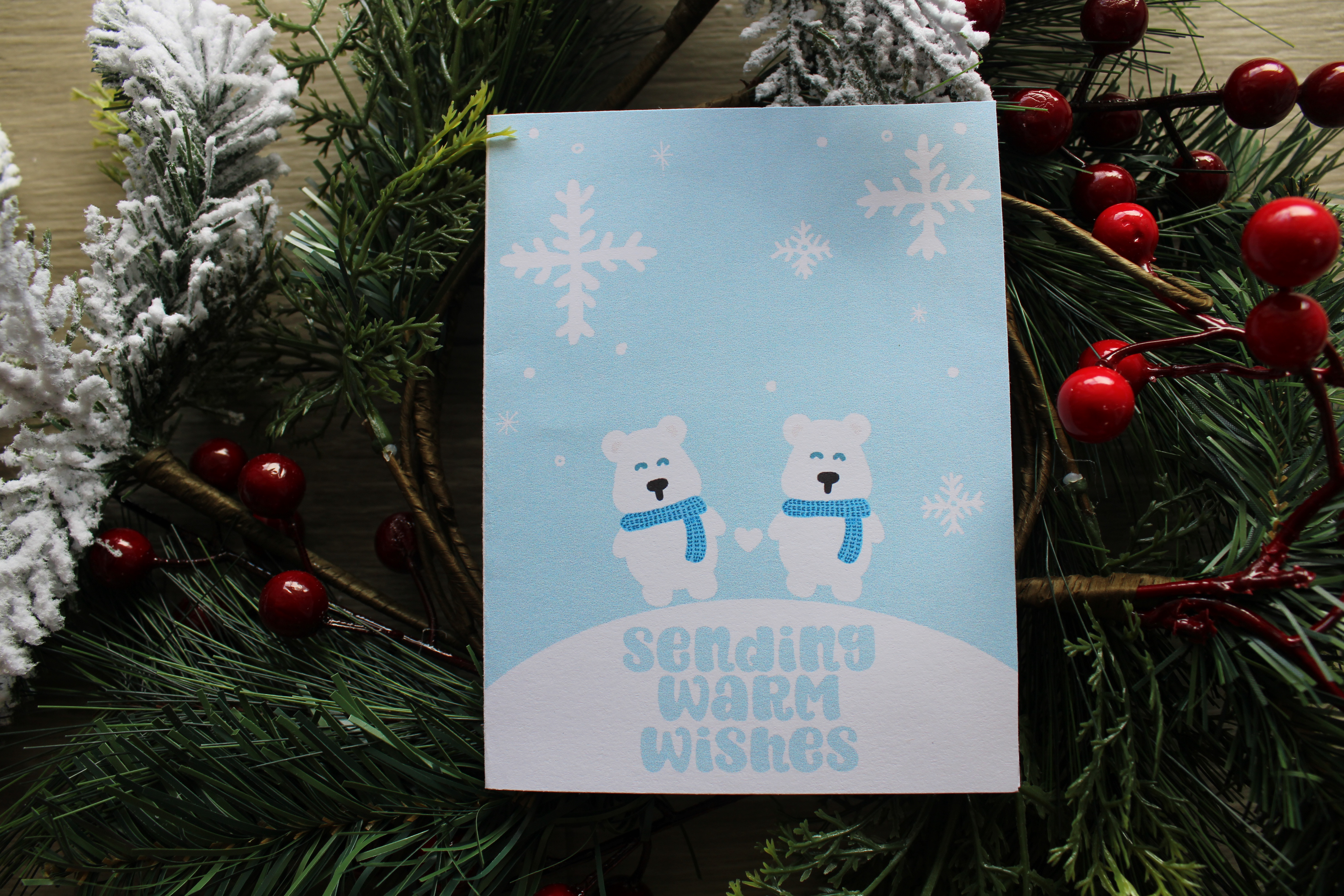 Greeting card with two bears wearing scarves and snowflakes, surrounded by festive decorations.